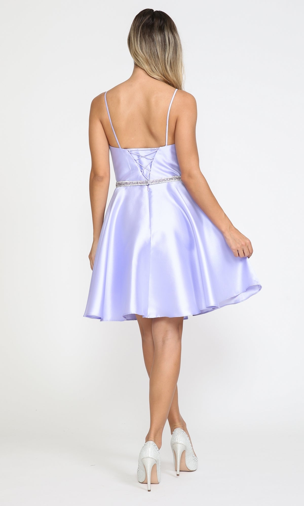 A woman in the Short Mikado Homecoming Dress 8420 with Pockets stands holding the skirt, showing off thin straps and a beaded waistband. Paired with white heels, this chic party look is perfect for any event and costs under $150.